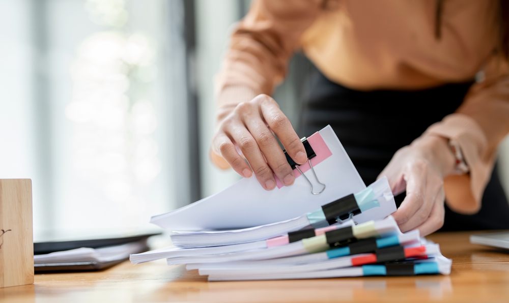 Businesswoman,hands,working,in,stacks,of,paper,files,for,searching